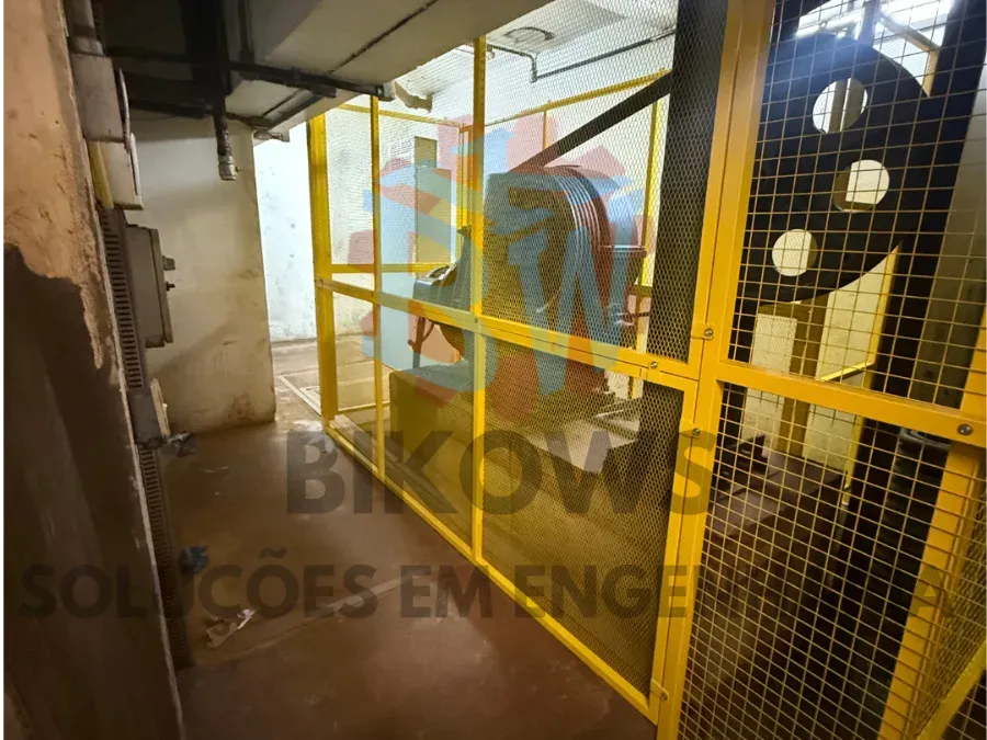 Corredor industrial com proteção em malha amarela e passarela elevada